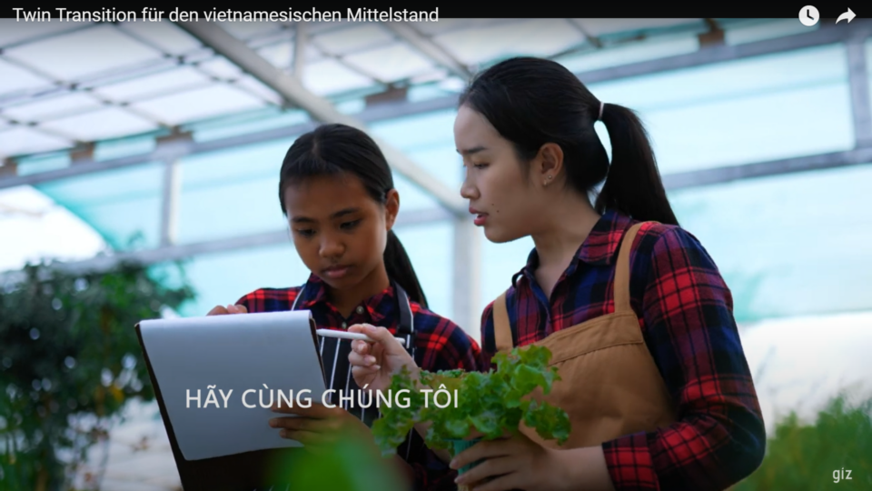Two women holding a tablet in a green house